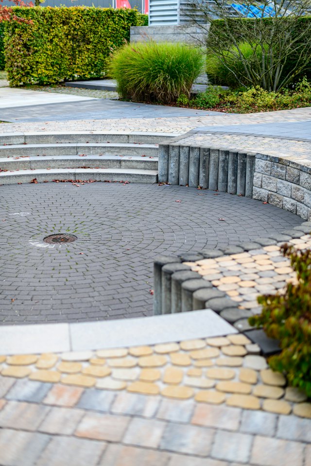 Een rond terras in kasseien met lage stenen treden en groen